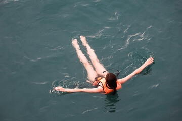 Girl in life vest swimming in sea water, top view