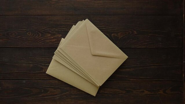 A stack of envelopes falls on a brown wooden table, top view