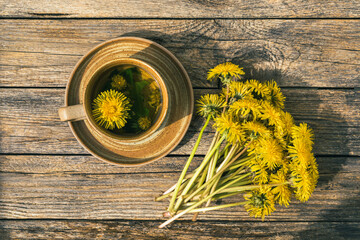 Ceramic mug of Dandelion tea with fresh flower on wooden background. Herbal medicine. Vitamin drink. Natural anti-inflammatory and antichloristic beverage for health. Atmospheric spring composition.
