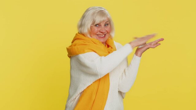 Senior woman showing wasting throwing sharing money around, more tips big profit winning lottery jackpot, successful shopping payment purchase cashback. Elderly mature grandmother on yellow background