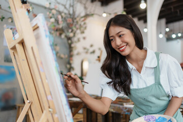 Asian female artist painter on canvas in creative studio as art. Cheerful young asian woman artist smiling drawing at art studio.