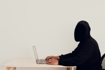 An anonymous hacker wears a hoodie over his head and is hacking into his victims' financial...