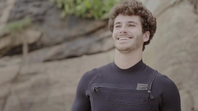 Jovem sorridente vestindo seu traje de surf. Cinematico 4k.