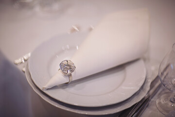 Plate for elegant wedding dinner. White napkin on white table. Beautiful table setting. A beautifully set table for a festive dinner. Wedding banquet. Plate, napkin with a ring.