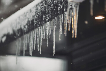 Icicles hang on the roof of a house. Spring landscape with icicles hanging from the roof of the...