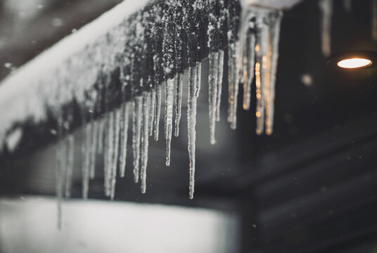 Icicles Hang On The Roof Of A House. Spring Landscape With Icicles Hanging From The Roof Of The House. Set Of Snow Icicles, Snow Hat. Soft Focus On Ice Icicle