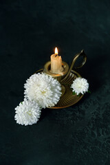 Burning candle in candlestick and white chrysanthemums flowers on black abstract backdrop. symbol...