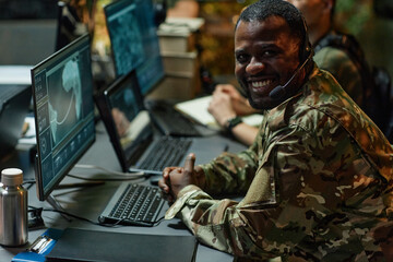 Happy young African American male military officer with headset looking at camera with smile while...