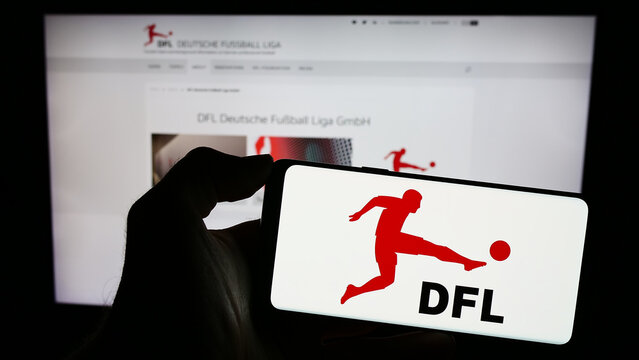 Stuttgart, Germany - 12-07-2023: Person holding mobile phone with logo of German football company DFL Deutsche Fußball Liga GmbH in front of web page. Focus on phone display.