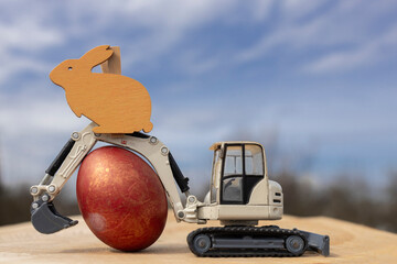 gray small toy excavator and an Easter egg against the sky. Easter holiday concept for construction companies