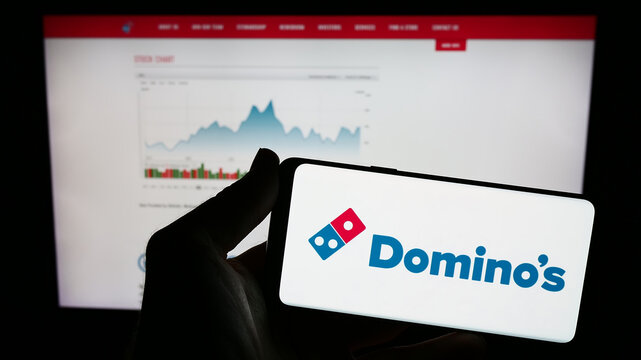 Stuttgart, Germany - 12-09-2023: Person holding mobile phone with logo of American restaurant chain company Domino's Pizza Inc. in front of web page. Focus on phone display.