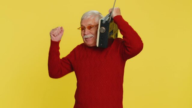 Senior old man using retro tape record player to listen music, disco dancing favorite track, having fun, entertaining, fan of vintage technologies. Elderly grandfather pensioner on yellow background