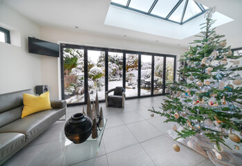 Bifold doors and skylight at Christmas in luxury room, xmas tree and view to garden with snow.