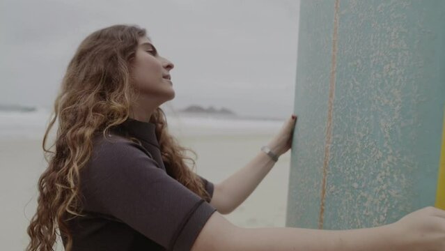 Young woman on the beach, concentrated, applying paraffin to her surfboard. Cinematic 4k.