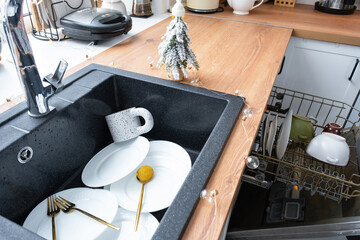 Dirty dishes in the sink in the garlanded kitchen, a holiday after a feast at Christmas. Mess after...