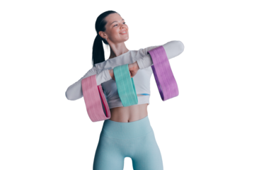 Cheerful Brunette girl in sportswear holds training rubber tapes smiles looks away happily satisfied by body shape. Fit young caucasian woman trains against transparent background. Women health.