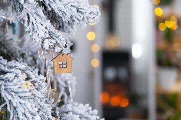 Key to the house with a keychain is hanging on the Christmas tree. A gift for New Year, Christmas. Building, design, project, moving to new house, mortgage, rent and purchase real estate. Copy space