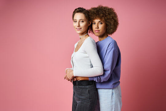 happy african american woman embracing her girlfriend on pink background, lgbtq couple love