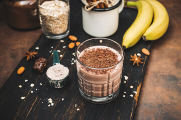 Milkshake smoothie, protein drink with grated chocolate in a glass on dark wooden board with...