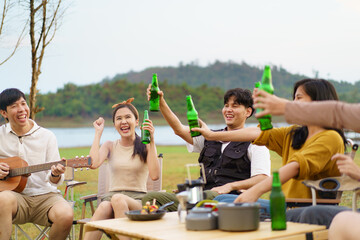 Asian young women and men celebrating with a bottle of a beer together.