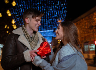 Valentines day concept, two young people in winter season on decorated city streets exchanging gifts 