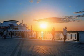 Deurstickers People are waiting to board a boat for a trip along the river. Walk along the embankment. Romantic sunset on the Volga River © oksanamedvedeva
