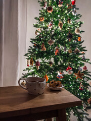 A cozy evening - a cup of tea, cookies on a wooden table against the background of a Christmas tree