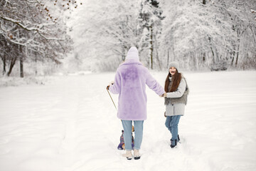 Mother and her daughter playing with their dog french bulldog on a snow