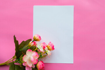 White mock up paper blank and bouquet of flowers on pink background. Valentine's Day or Mother's Day greeting card