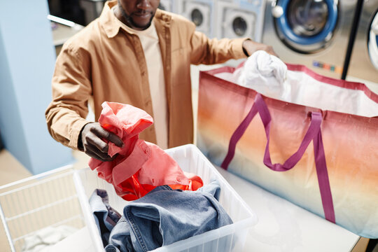 Hand Of Young African American Man In Beige Shirt Putting Denim Jacket And Pink Attire Into Plastic Container Before Washing His Clothes