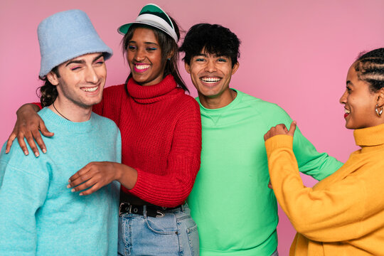 Group of four friends in vivid sweaters smiling together with a pink background