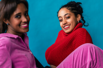Two women in red and pink attire share a close, radiant, and cheerful moment together