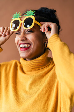 Woman in yellow turtleneck poses playfully with pineapple sunglasses