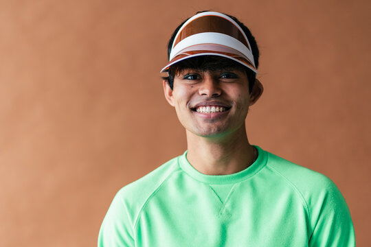 Man in green sweater with visor cap smiling widely, teeth showing