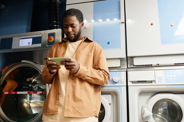 Young African American man marking time of washing in his smartphone or watching online video while...