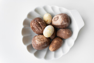 On a white scalloped plate lie chocolate eggs that are already coated with a coating of stitched chocolate. Various types of chocolates.