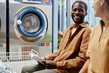 Happy young African American man with open book looking at girl in laundry while discussing novel...