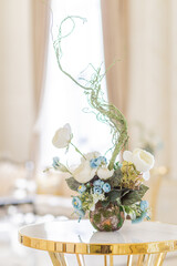 Table decorated with a vase with a bouquet of flowers in a luxurious light gold interior.