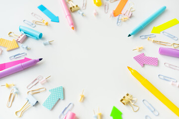 Colorful assortment of office supplies including pens, markers, paper clips and paper clips scattered on a white background. The overall mood is bright and creative, with space for writing.