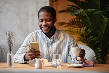 Young African American entrepreneur looking at smartphone screen with smile during communication in...
