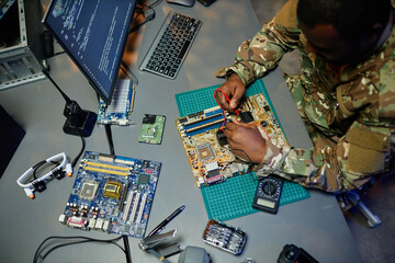 Above angle of young African American man in military uniform repairing motherboard with...