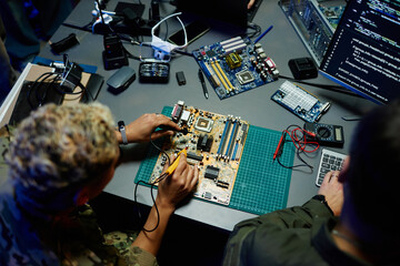 Above angle of young female officer in military uniform repairing motherboard with transmission...