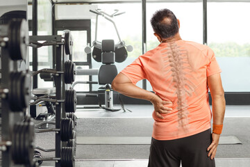 Rear view shot of a man holding his painful back at the gym