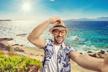 Young man with a straw hat and glasses taking a selfie by the sea