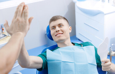 Young happy man client and dentist giving high five to each other in dentistry. Good work is done,...