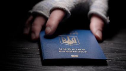 Close up shot of person identity document. Shot of male hand placing blue Ukrainian passport with national symbols on the table.