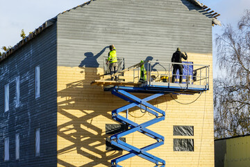 Residential house facade painting works after cladding with wooden planks using scissor lift...