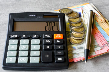 Calculator with number 2024 on display, pen, euro banknotes and coins on grey background