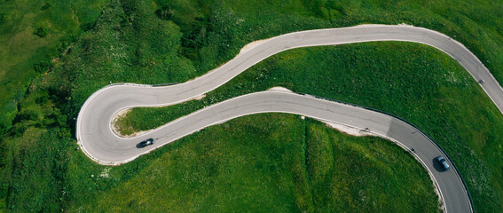 Passo Gardena Green hills Aerial drone shot of curved mountainous road with cars passing through...