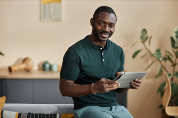 Waist up portrait of smiling African American man holding digital tablet and smiling at camera in...